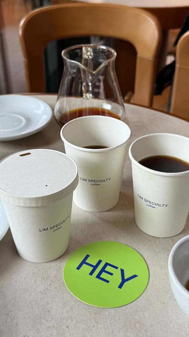 The first HEYLIM cups beside the green HEY coaster on a café table